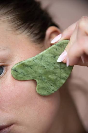 Pedra de gua sha em jade a deslizar sobre a face, na direcção do maxilar para a orelha