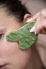 Pedra de gua sha em jade a deslizar sobre a face, na direcção do maxilar para a orelha
