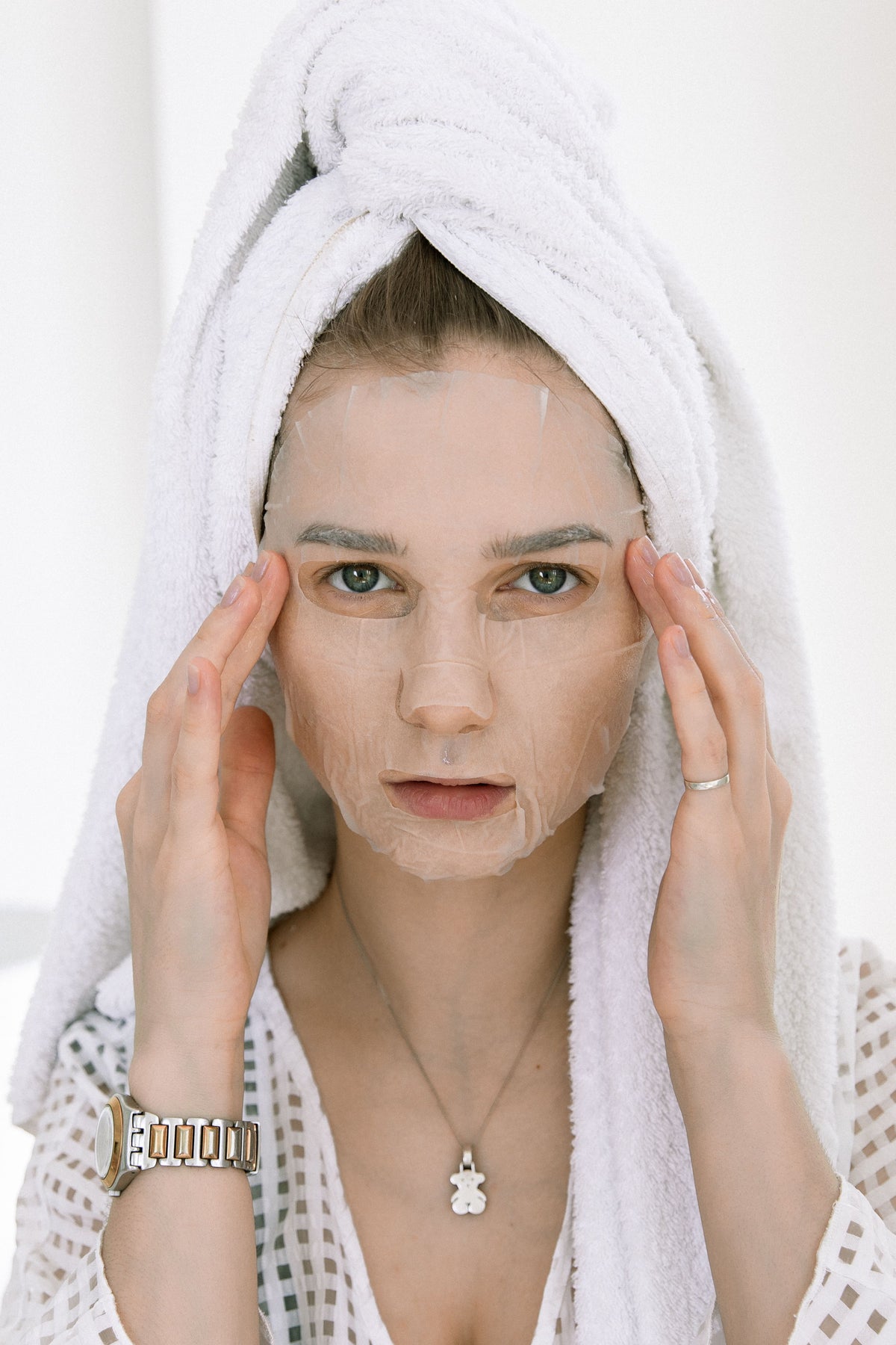 Mulher com máscara facial e toalha na cabeça.